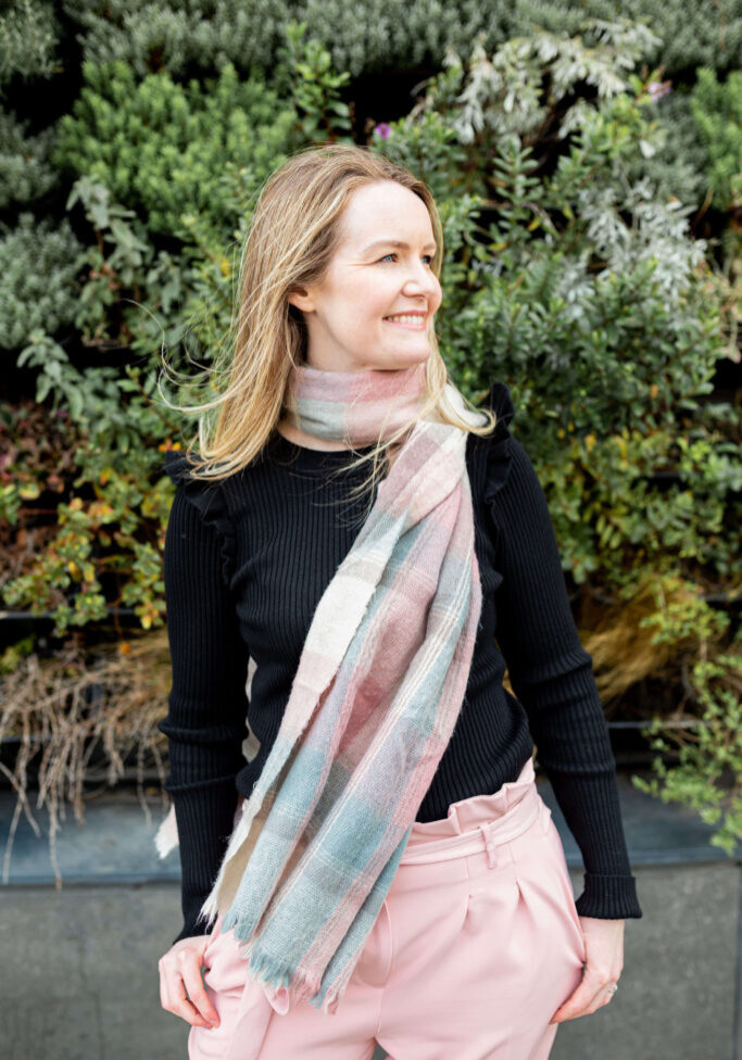 laura greenwood smiling on a windy day with pink and blue scarf blowing in the wind